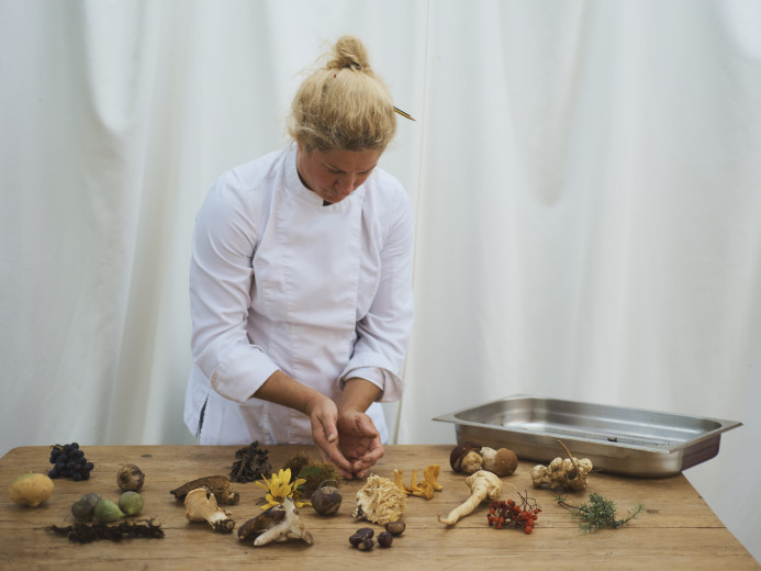 Ana Roš bent over a table covered with mushrooms and other vegetables.