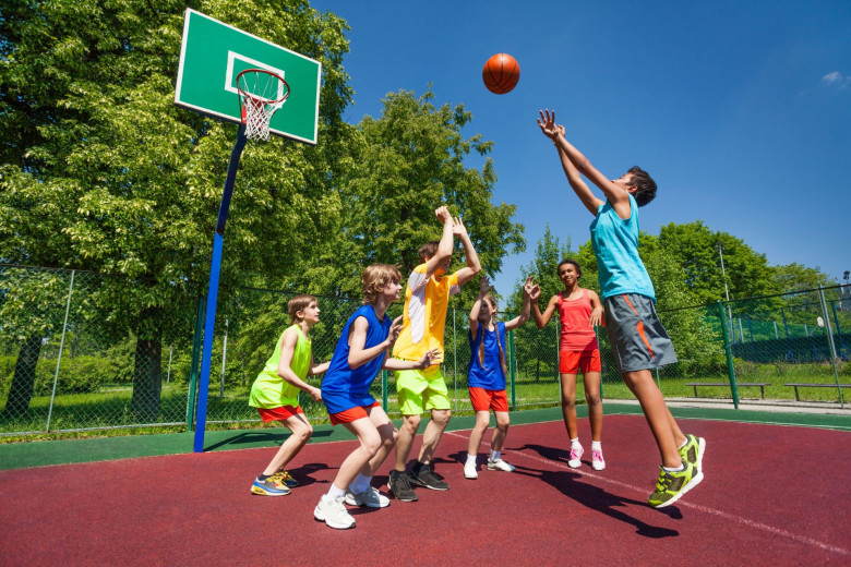 Dečki igrajo košarko na igrišču.