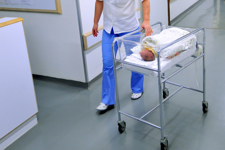 A maternity hospital employee wheels a newborn baby in a trolley.