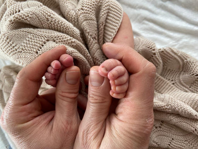 The adult hands hold the baby's feet.