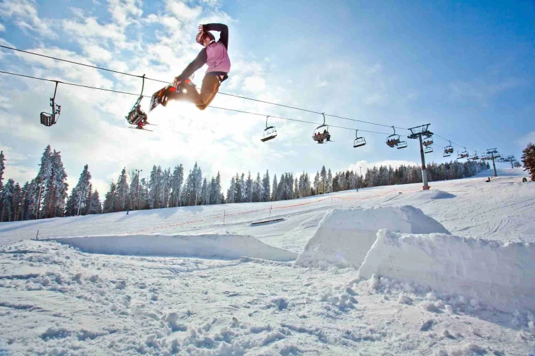 A girl has her ski board on and is wearing ski equipment. She is on a snowy slope on a sunny day and jumping high in the air.