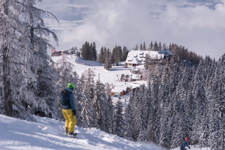 In the foreground, a skier on a board watches the Krvavec ski slope.