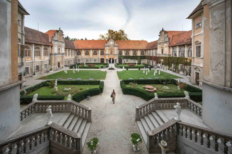 Statenberg Castle, with the castle garden in the foreground. The garden is surrounded by the building and in the front are stairs with statues on the left and on the right.