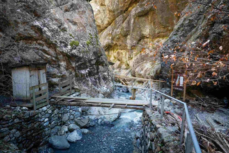 A footbridge over a river in a gorge, surrounded by stone walls.