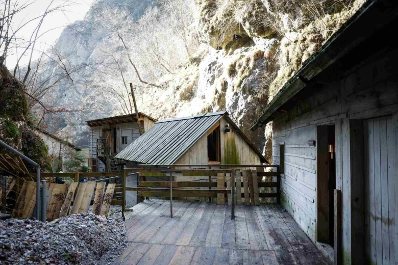 Franja Hospital, depicting small wooden houses close to one another on different levels. A rocky hill is in the background.