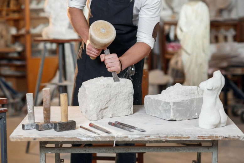 A stonecutter shapes a stone with a chisel.