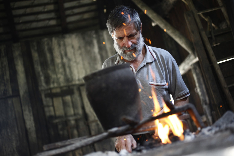 A blacksmith shapes a product by the fire.