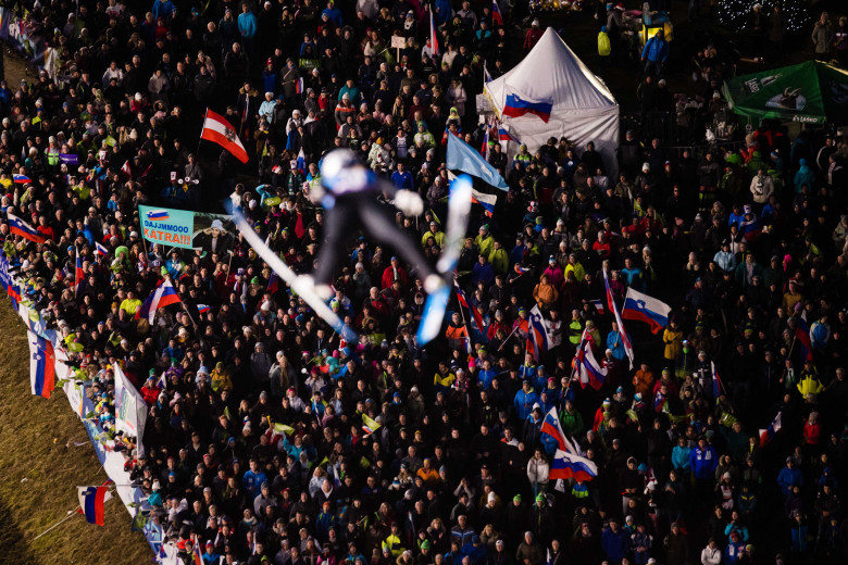 A jumper in the air, a crowd with flags below.