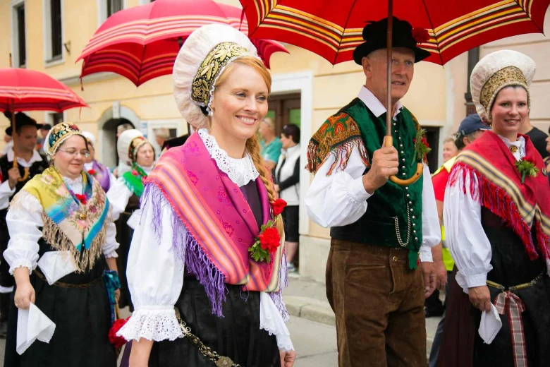 A couple in a colorful Gorenjska national costume is walking in a procession. The man is holding an umbrella.