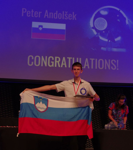 Andolšek na zmagovalnem odru drži slovensko zastavo.
