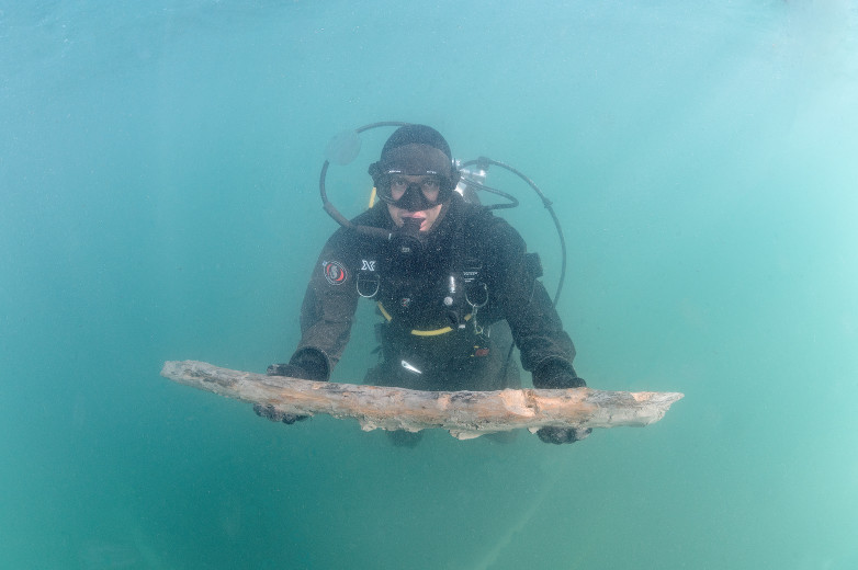 A diver holds a mast in the water.