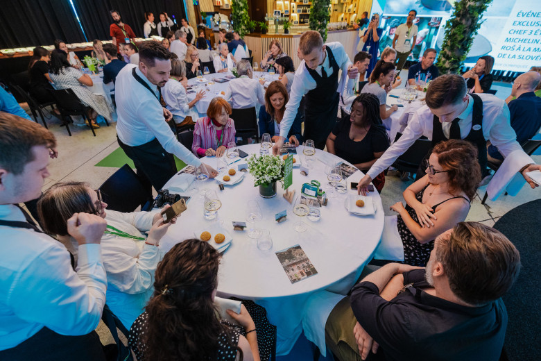 Several waiters serve guests at a round table at an event.