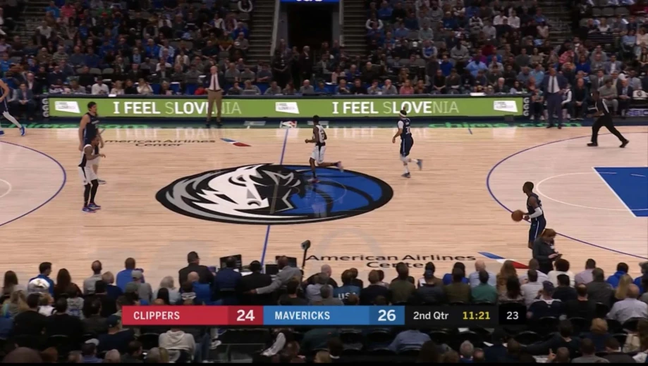 A screenshot of television streaming a basketball game. There is a red-blue board with a score written on it under the court. It says Clippers 24 against Mavericks 26. 