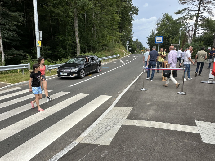 Deklici na prehodu za pešce, pred njim stoji avto, ob strani se sprehajajo ljudje.