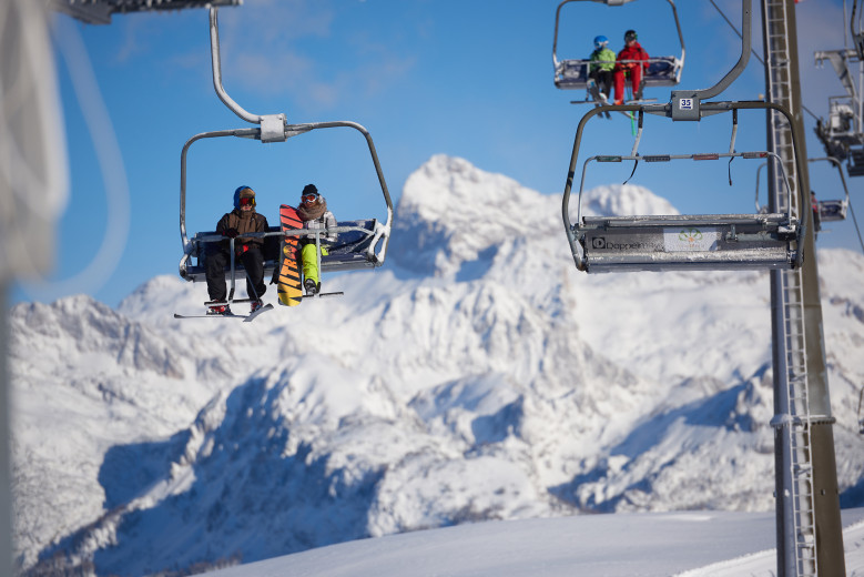 A chairlift with skiers in the foreground, mountains in the background.