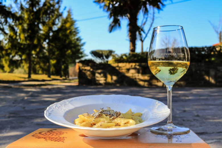 A plate with pasta and truffles and a glass of white wine.