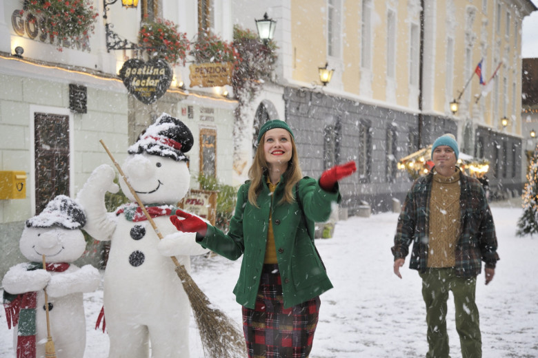A woman stands next to two snowmen.