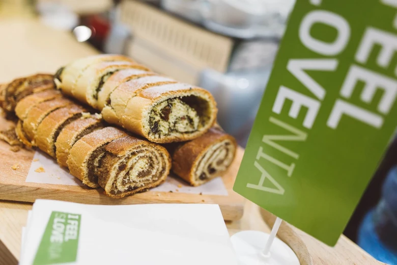 Sliced potica cake is displayed on a wooden board on the table, Green I Feel Slovenia flag is by the side.