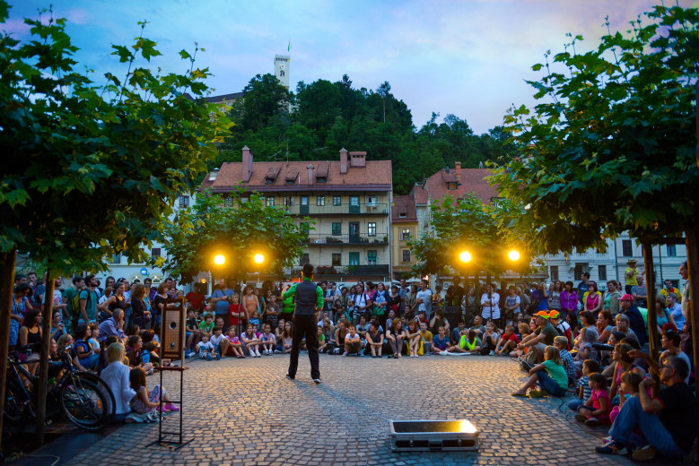 Gledalci na ulici gledajo nastop igralca v starem mestnem jedru Ljubljane. 