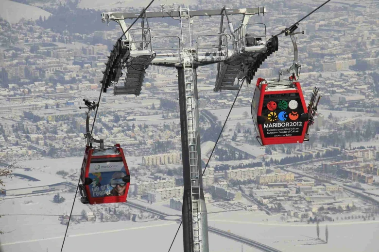 Two gondolas are going up and down over snow-covered Maribor.