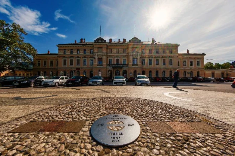 V ozadju železniška postaja v Novi Gorici, v ospredju sončna ura.