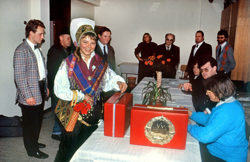 A girl in Slovenian national costume in front of a voting booth.