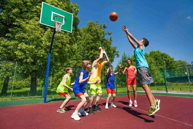 Kids are playing basketball on a court outside. One of them just jumped and threw the ball.