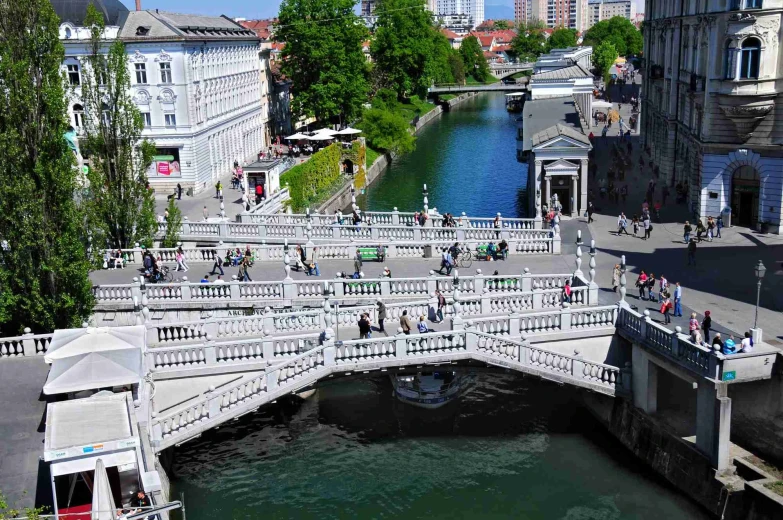 An aerial view of Ljubljana triple bridge in the centre and people walking across it. Under it flows Ljubljanica river.