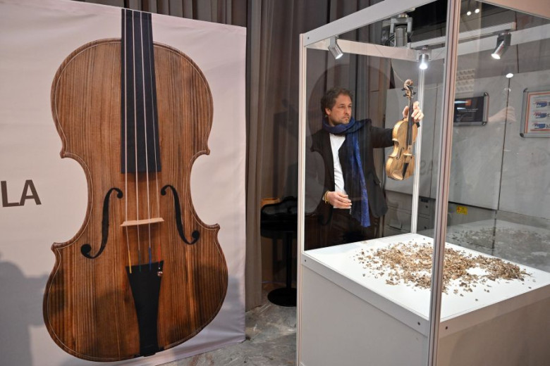 A man holding a violin standing in front of a poster of a violin.