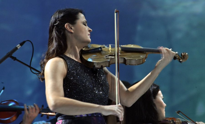 Woman in sparkly black dress play the violin. 