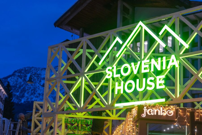 Green neon sign Slovenia house on a wooden construction at night.