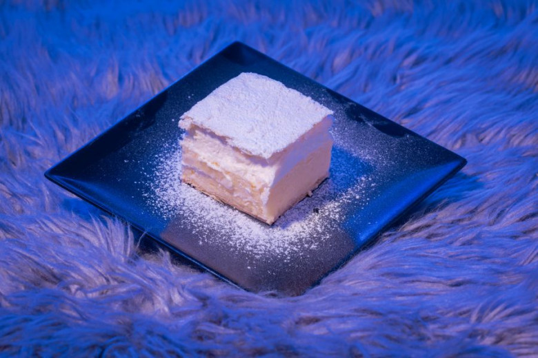 Bled cream cake on a dark platter in illuminated with blue light.