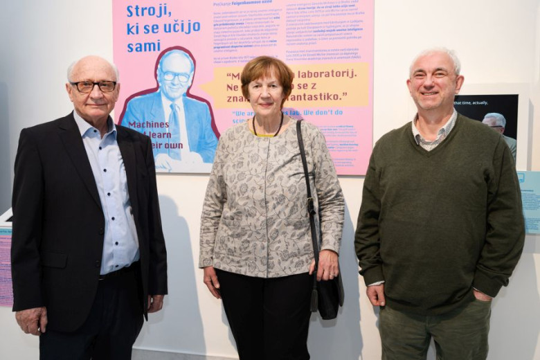 Ivan Bratko, Nada Lavrač in Saša Džeroski are standing in front of colorful exhibition panels with text about machine learning.