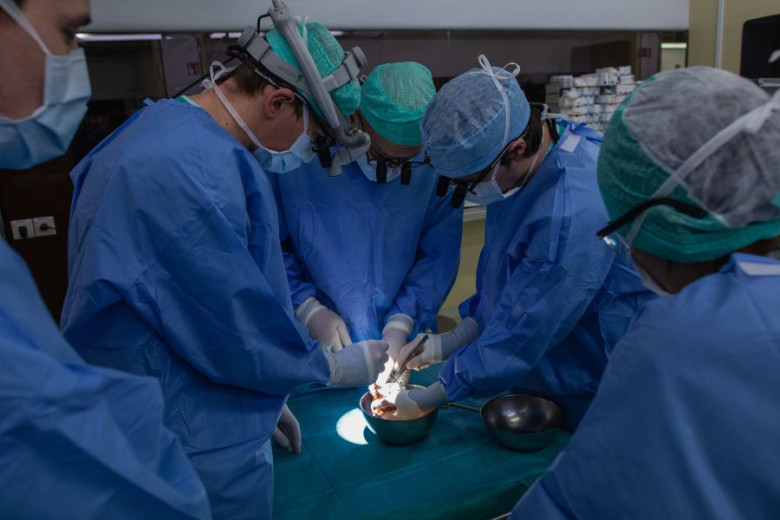 Surgeons in blue scrubs and masks perform a precise operation under focused lights.